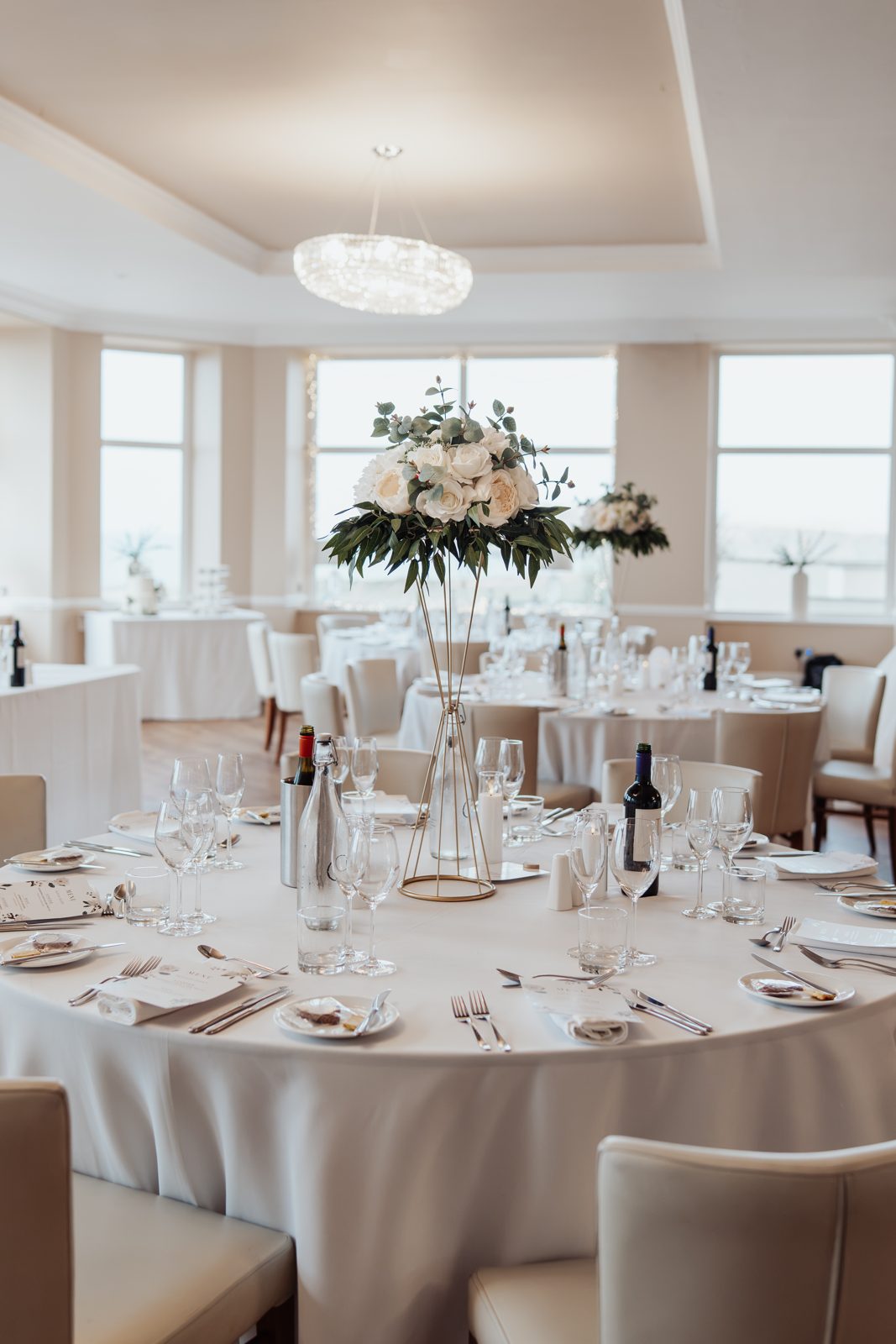 Tall ivory rose and peony arrangement on a gold stand at a wedding reception table